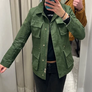 Grön vårjacka med dragkedja - Snygg grön vårjacka med fyra stora fickor framtill och dragkedja. Jackan har klassisk krage och raka ärmar. Perfekt för dig som gillar en stilren och funktionell look.