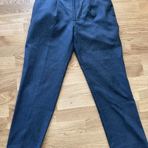 Mörkgrå kostymbyxor från Bläck - Snygga mörkgrå kostymbyxor från Bläck med klassisk rak passform. Byxorna har diskreta bakfickor, dragkedja och knäppning fram. Säljer då de inte sitter så bra på mig och de förtjänar mer användning. Summen har släppt lite på ena benet (bild 4) men går enkelt att laga.