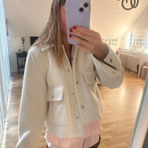 Vit overshirt jacka från Zara - Säljer en stilren vit overshirt jacka från Zara med stora fickor framtill och knappar. Jackan har klassisk krage och lång ärm, perfekt för lager-på-lager. Materialet känns mjukt och ger en clean look.