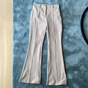 Beiga kostymbyxor från SHEIN - Snygga beiga kostymbyxor från SHEIN med hög midja och raka pressveck. Byxorna har en klassisk passform med bootcut och stängs med knapp och dragkedja. Perfekta för en stilren look.