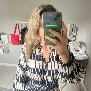 Mönstrad kortklänning från MNG - Säljer en snygg kortklänning från MNG med svart och beige mönster. Klänningen har långa puffärmar, markerad midja med resår och knappar framtill. Perfekt för dig som gillar unika mönster och bekväm passform.