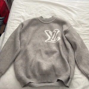 Stickad LV tröja - Säljer en grå stickad tröja från Louis Vuitton med stort vitt LV-logotyp på bröstet. Tröjan har rund halsringning och långa ärmar. Perfekt för dig som vill ha en stilren och exklusiv look. Priset kan diskuteras vid snabb affär. 