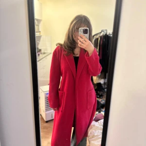 Rosa kappa med bälte - Säljer en snygg rosa kappa med bälte i midjan och stora fickor framtill. Jackan har lång ärm och klassisk krage, perfekt för att ge en färgklick till din outfit. Enkel att styla och superbekväm.