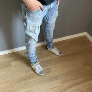 Ljusblå jeansbyxor från Nudie Jeans - Säljer ett par ljusblå jeansbyxor från Nudie Jeans med klassisk femficksdesign och orange sömmar på bakfickorna. Jeansen har normal passform och raka ben, perfekta för en avslappnad stil. Den är liten spänd på vissa ställen pris inte hugget i sten !! Kille som står där är 170cm och väger ca 55-60kg