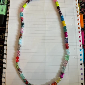 Färgglatt pärlhalsband - Ett långt halsband med pärlor i många olika färger, perfekt för att liva upp vilken outfit som helst. Pärlorna är runda och varierar i nyanser som blå, rosa, gul, grön, lila och fler. Halsbandet har en lekfull och trendig känsla.