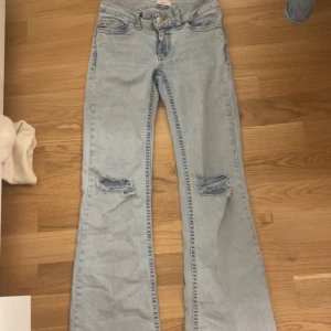Ljusblå bootcut jeans med hål på knäna och rosa detaljer  - Säljer ett par ljusblå bootcut jeans med hål på knäna och broderade detaljer på bakfickorna. Jeansen har normal passform och Perfekta för dig som gillar en avslappnad och trendig stil. Använt typ 5 gånger. storlek 32. Säljer för 400,köpte för 699. PRISET KAN DISKUTERAS.