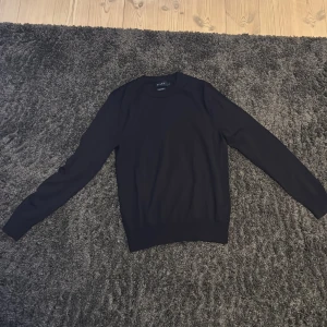 Mörkblå merinoulltröja från Riley - Säljer en klassisk mörkblå långärmad tröja från Riley i mjuk merinoull. Perfekt basplagg med rund halsringning och enkel design. Passar till många olika stilar och är riktigt skön att ha på sig.