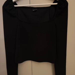 Svart långärmad topp med fyrkantig ringning - Säljer en svart långärmad topp med snygg fyrkantig ringning och puffiga axlar. Toppen har en tight passform och är perfekt att styla till olika outfits. Använd vid två tillfällen! 
