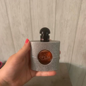 Black Opium Eau de Parfum från Yves Saint Laurent - Säljer en Black Opium parfym från Yves Saint Laurent. Flaskan är silverglittrig med rund orange detalj i mitten och svart rund kork. En ikonisk doft i snygg och lyxig design. Endast testad 1 gång så den är som ny!