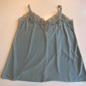 Grön linnetopp med spets från Amisu - Säljer en ljusgrön linnetopp från Amisu med tunna axelband och vacker spetsdetalj längs urringningen. Toppen har en mjuk och följsam känsla, perfekt för varma dagar eller lager på lager.