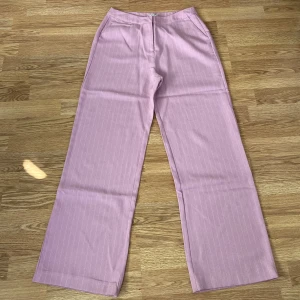 Ljusrosa kostymbyxor från NLY Trend - Säljer ett par ljusrosa kostymbyxor från NLY Trend med diskreta vita ränder. Byxorna har raka vida ben och sidfickor. Perfekta för dig som gillar en stilren och trendig look.