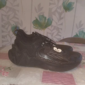 Svarta sneakers från nike - Säljer ett par svarta sneakers från nike med coola vita detaljer och mönstrad sula. Skorna har snörning och tydliga nike-loggor på plösen och hälen. Perfekta för dig som vill sticka ut med en unik och trendig look.