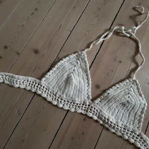 Beige virkad croppad linnetopp - Säljer en handvirkad beige linnetopp med knytband i nacken och runt ryggen. Toppen har en triangelformad design och är croppad, perfekt för sommaren. Hade valet super snyggt till ett par shorts 