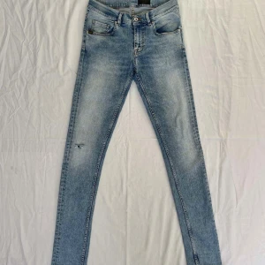 Ljusblå jeans från tiger of Sweden - Säljer ett par ljusblå jeans från Angel of Sweden. Jeansen har klassisk femficksdesign, slitning på ena benet och smal passform. Perfekta för dig som gillar en tajt look och vill ha ett par jeans med lite edge.