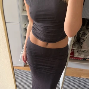 Svart tvådelad långklänning - Säljer en mörkgrått set med tight passform. Klänningen består av en crop top och en lång kjol i ett stretchigt material. Perfekt för dig som vill ha en stilren och trendig look. Storlek S 