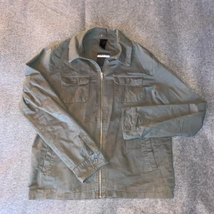 Censored overshirt  - En grön overshirt med dragkedja framtill och två bröstfickor med knappar. Riktigt snygg och stilren.