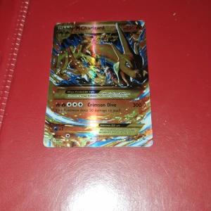 Pokémonkort M Charizard EX - Säljer ett Pokémonkort av typen M Charizard EX med holografisk yta. Kortet har en färgstark design med Charizard i svart och blått, samt guldiga detaljer. Text och symboler är tydliga och kortet har en klassisk Pokémon-baksida.                                                     Obs hämtas upp här eller i Älmhult 