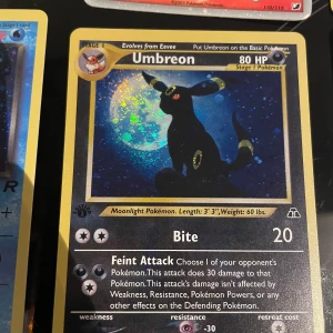 Pokémonkort Umbreon - Säljer ett samlarkort från Pokémon med Umbreon-motiv. Kortet har en mörk bakgrund med Umbreon framför en måne. Texten är på engelska och kortet har 80 HP. Perfekt för samlare eller Pokémon-fans!