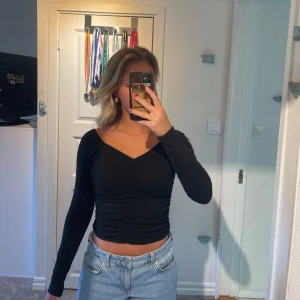 Svart croppad långärmad topp med v-ringning - Säljer en svart croppad topp med lång ärm och snygg v-ringning. Toppen har rynkade detaljer framtill som ger en schysst passform.