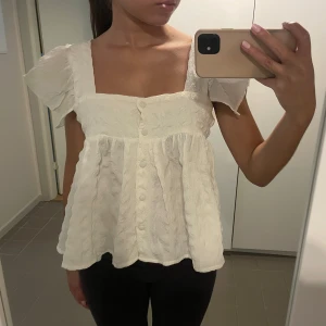 Vit blus med volangärmar - Säljer en söt vit blus/linne med korta volangärmar och knappar framtill. 