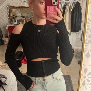 Svart ribbad croppad topp med cut-out axlar - Säljes en mörkgrå ribbad topp med långa ärmar och cut-out detaljer vid axlarna. Toppen är ifrån Zara och är väldigt eftertraktad. Jag har lagat toppen som syns på bild 3, detta syns dock inte vid andvänding. 