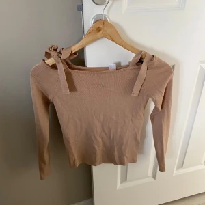 Beige topp med knytband från H&M Divided - Säljer en beige långärmad topp från H&M Divided med knytband på axlarna. Toppen har en tight passform och är tillverkad i mjuk bomullsmix. Perfekt för en stilren och trendig look.