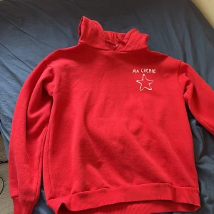 Röd hoodie från Gina Tricot med text och stjärna - Röd hoodie från Gina Tricot med vit broderad text 'MA CHÉRIE' och en stjärna på bröstet och ryggen. Mjuk insida och ribbade muddar vid ärmslut och nederkant. Perfekt för dig som gillar färg och enkel design. Använd några gånger.