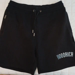 Svarta shorts från Hoodrich - Svarta shorts från Hoodrich med vit logga på vänster ben. De har snörning i midjan och är tillverkade i ett mjukt material som passar perfekt för avslappnade dagar.
