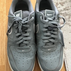 Grå Nike Air Force sneakers - Säljer ett par grå Nike Air Force sneakers med klassisk design och vit swoosh på sidan. Skorna har snörning, rund tå och perforerade detaljer framtill för extra ventilation. Perfekta för dig som gillar stilrena och tidlösa sneakers. Har köpt de för 1200kr och säljer de för bara 500kr ( vid snabb affär kan priset diskuteras)