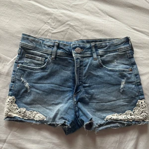 Blå jeansshorts med spetsdetaljer - Snygga blå jeansshorts med slitningar och vita spetsdetaljer längst ner på benen. 