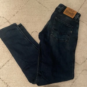 Mörkblå Replay Anbass jeans - Säljer ett par mörkblå Replay Anbass jeans i storleken 28/32 med en klassisk femficksdesign och snygga slitningar. Jeansen har en slim passform, dragkedja och är tillverkade i stretchigt denim för extra komfort. Perfekta för dig som gillar stilrena och tidlösa jeans. Hör av dig vid minsta fundering 