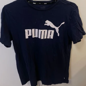 Mörkblå t-shirt från Puma - Snygg mörkblå t-shirt från Puma med klassisk vit logga och tryck framtill. T-shirten har rund halsringning och korta ärmar. Perfekt för en sportig och avslappnad stil.