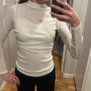 Vit glittrig meshtröja med lång ärm - Säljer en tunn, vit meshtröja med diskret glittereffekt och lång ärm. Tröjan har hög hals och är figurnära i modellen. Perfekt att styla lager på lager eller som statement-piece till din outfit.