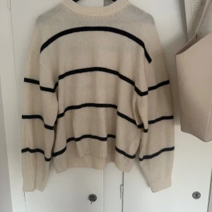 Vit och svart randig stickad tröja - Säljer en vit stickad tröja med svarta ränder. Tröjan har lång ärm, rund halsringning och ribbade muddar vid ärmslut och nederkant. Skriv vid en intresse eller funderingar!❤️