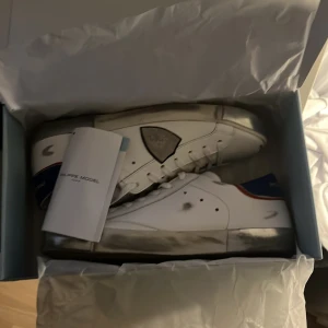 Snygga Philippe model sneakers - Säljer ett par vita Philippe Model sneakers med blå häl och röda detaljer. Skorna är sprillans nya aldrig använda skicka 10/10. Kvitto från merchsweden finns