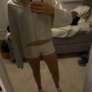 Ljusgrå croppad stickad tröja från Gina Tricot - Mysig ljusgrå stickad tröja från Gina Tricot med v-ringning och croppad passform. Tröjan har långa ärmar och breda muddar vid ärmslut och nederkant. Perfekt för lager-på-lager och chill dagar.