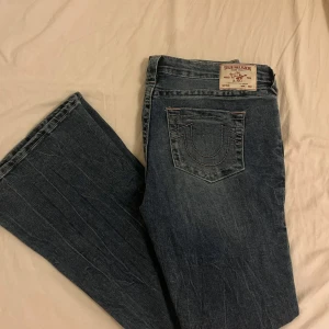 True Religion Ultra Low Rise Flare Jeans - Säljer ett par blåa jeans från True Religion med ultra låg midja och utsvängda ben. Klassisk femficksmodell med tydliga sömmar och ikoniska bakfickor. Säljer pågrund av för stora i midjan. Passar mig som är 177 cm. 