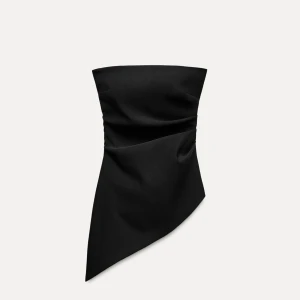 Svart asymmetrisk tubtopp - Säljer en svart tubtopp med asymmetrisk nederkant och stilren design. Toppen är axelbandslös och har en snygg drapering framtill. Perfekt för dig som vill ha en trendig och unik look.