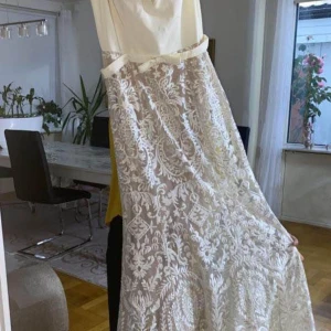 Beige/ vit långklänning med spetsmönster  - Säljer en elegant vit långklänning med vackert broderat spetsmönster över hela klänningen. Klänningen har ärmlös design och en klassisk, figurnära passform som ger en lyxig känsla. Passar till studentbalen Priset kan diskuteras vid snabb affär 