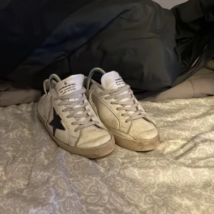 Vita sneakers från Golden Goose med svart stjärna - Golden Goose sneakers i vitt skinn med svart stjärndetalj på sidan. Jag säljer dessa skor eftersom att jag inte har någon användning för dem längre.