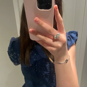 Mörkblå blus med volangärmar - Säljer en mörkblå blus med broderade detaljer och volang vid axlarna. Blusen har korta ärmar och är tillverkad i ett lätt material som passar perfekt till vår och sommar.