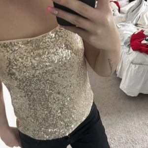 Guldig paljettlinne med smala axelband - glittrigt guldigt linne med paljetter och smala axelband. Perfekt för att sticka ut och ge extra bling till outfiten. Linnet visar inte tecken på mycket användning! Superfin till festligare tillfällen! 