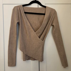 Beige ribbad omlottopp - Säljer en beige ribbad omlottopp med lång ärm. Toppen har en djup v-ringning och omlottdesign framtill som ger en snygg och trendig look. Aldrig använd