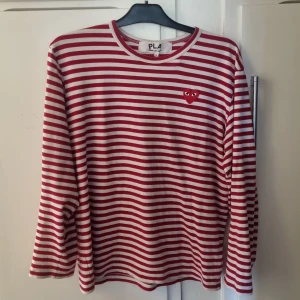  Comme des Garçons Play - tröja  - Säljer en klassik röd och vit randig långärmad tröja från Comme des Garçons Play. Tröjan har ett broderat rött hjärta på bröstet och är tillverkad i 100% bomull. Perfekt för dig som gillar klassisk och stilren design. Mycket bra skick. 