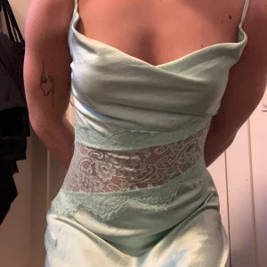 Ljusgrön satinklänning med spetsdetaljer - Säljer en ljusgrön satinklänning med smala axelband och vackra spets detaljer. Klänningen har en elegant, figurnära passform och är tillverkad i glansigt satinmaterial. Perfekt för bal! Helt oanvänd. Köpt i usa. Det finns små defekter som finns med på sista bilden. Nästan omärkbart, tror de kan vara från min katt när den bara hängt i min garderob.