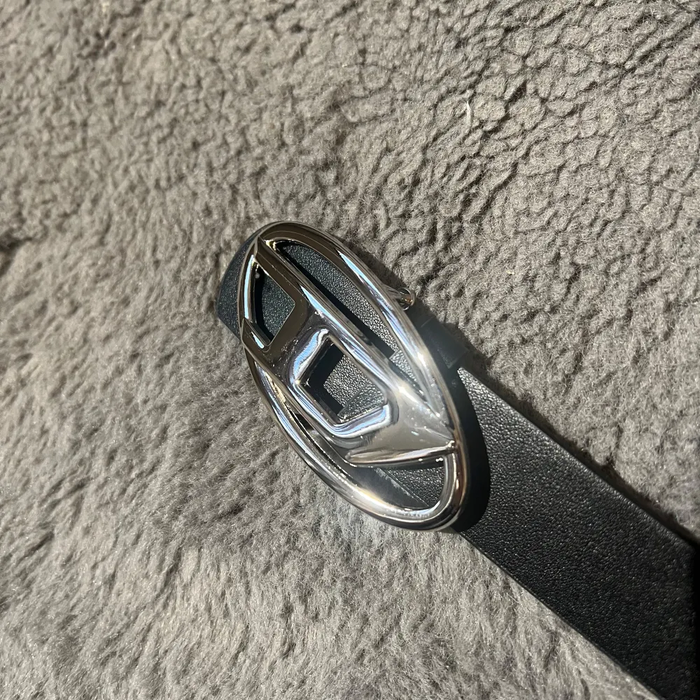 Snyggt svart bälte i skinn med ett stort, Skick 9/10. Färg: Svart och silver. Storlek 105 cm, bältet har flera hål för justerbar passform.. Asusteet.