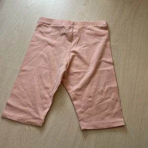 Ljusrosa cykelbyxor från H&M - Säljer ett par ljusrosa cykelbyxor från H&M. Byxorna är knälånga och har en mjuk resår i midjan. Perfekta för träning eller som ett bekvämt basplagg. Tillverkade i bomull med lite stretch för extra komfort.