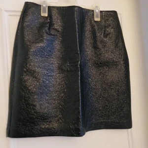 Svart kjol i skinnimitation från Lindex - Säljer en svart, glansig kjol i skinnimitation från Lindex. Kjolen har en rak passform och är kort i modellen. Perfekt för dig som gillar en stilren och edgy look.