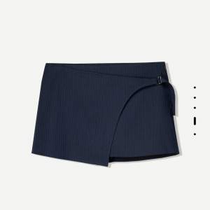 Snygg mörkblå omlottkjol från Bershka med diskreta ränder och spänne i sidan. Kjolen har en kort passform. Har inbyggda shorts och är helt ny. Köptes för 350