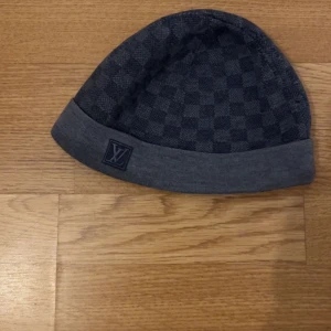Grå rutig mössa från Louis Vuitton - Snygg grå mössa med diskret rutigt mönster och uppvikt kant. Märkt med Louis Vuitton-logga framtill. Perfekt accessoar för kyligare dagar. ÄKTA 